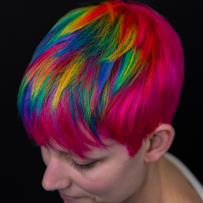 Young woman with short, textured pixie haircut in neon pink with prism rainbow colour blocking, created using Danger Jones hair colour.