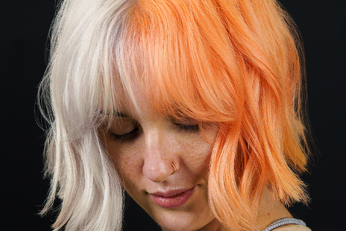 Young woman with chin-length textured bob with curtain fringe and tousled beach waves, split-dyed half platinum white blonde and half peach using Danger Jones peach colour.