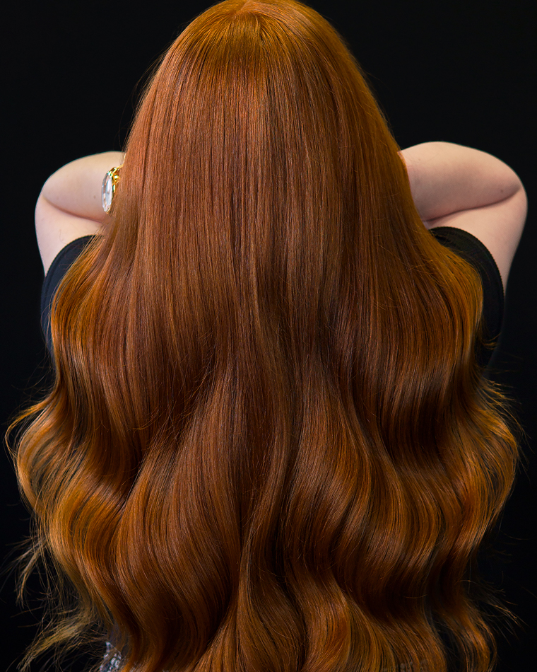 Young woman with rich copper-red hair with golden tones, a glossy finish, and large, flowing waves.