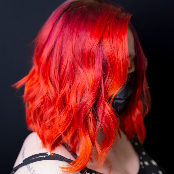 woman with bright fire red curly hair in salon with dark background pulp riot