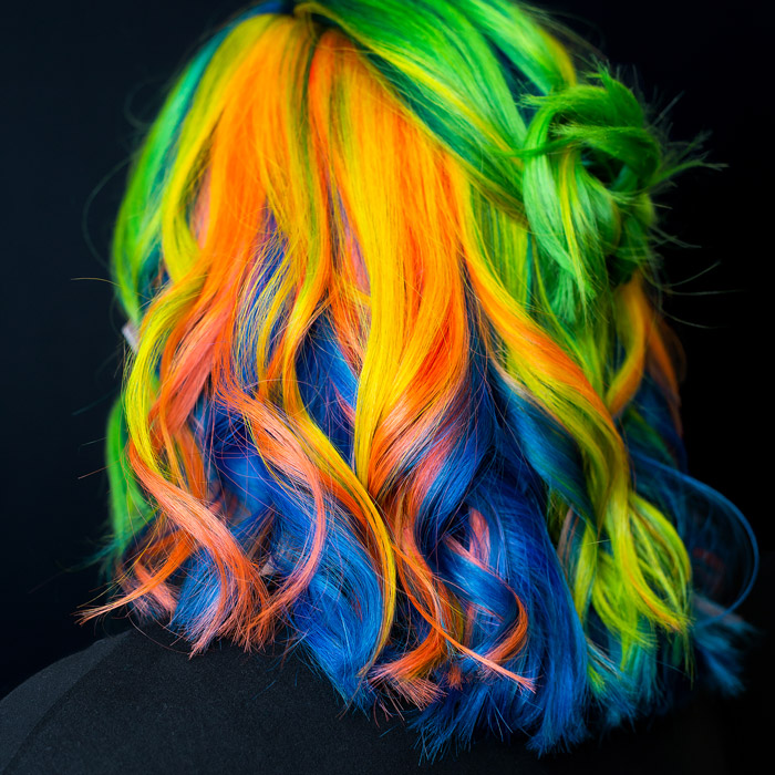 young woman with curly hair dyed bright yellow, orange and blue in hair salon pulp riot