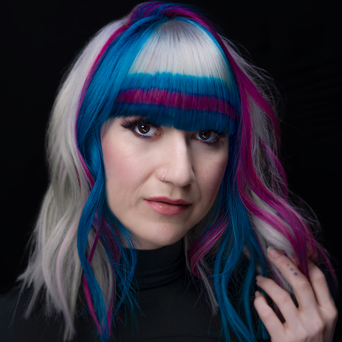 Young woman with platinum white blonde hair featuring an intricate band of horizontal and vertical neon blue and pink stripes, created using Danger Jones hair colour.
