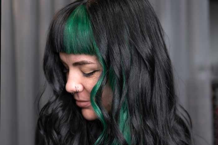 Young woman with black hair and emerald green colour blocking through half the fringe and the money piece section on her left, using Danger Jones hair colour.