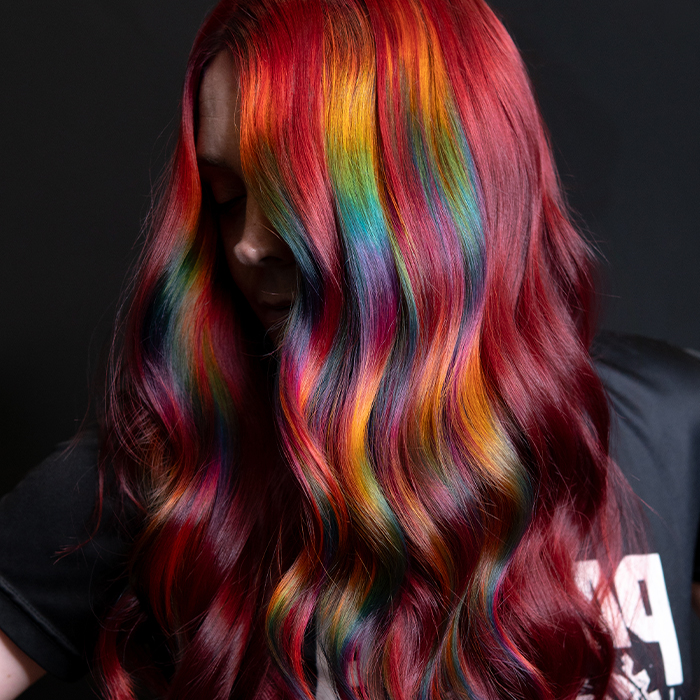 Young woman with vibrant red hair accented by panels of rainbow prism colour, created using Danger Jones hair colour.