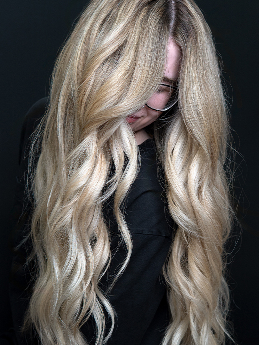 Young woman with long, wavy champagne blonde hair with creamy platinum highlights, sandy beige dimension, and a softly blended shadow root.